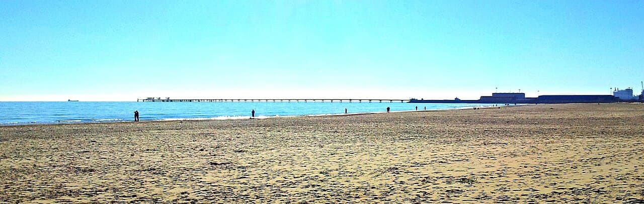 Het strand van Port de Sagunt, met de pier en de haveninstallaties op de achtergrond